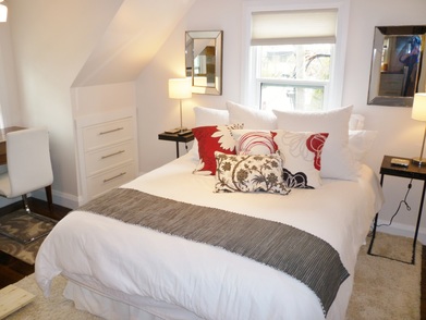 studio apartment bedroom with white bed linens and red pillows